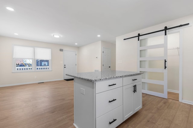 kitchen featuring a kitchen island, white cabinetry, light stone counters, a barn door, and light wood-type flooring