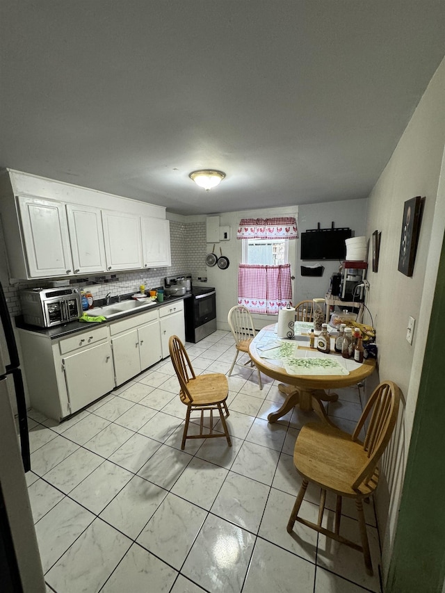 kitchen with stainless steel appliances, backsplash, light tile patterned floors, sink, and white cabinetry