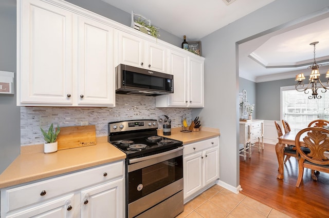kitchen featuring light tile patterned floors, white cabinetry, a tray ceiling, stainless steel range with electric cooktop, and decorative backsplash