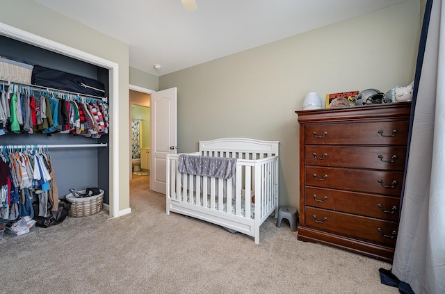 bedroom with ceiling fan, a closet, light colored carpet, and a nursery area
