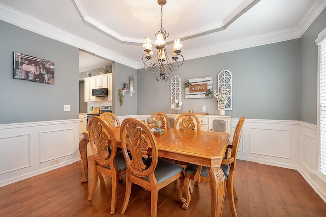 dining space with wood-type flooring, a tray ceiling, a notable chandelier, and ornamental molding