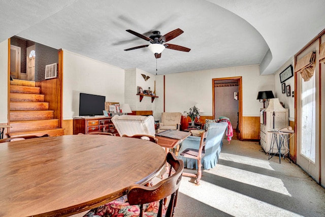 carpeted dining area with ceiling fan and wood walls