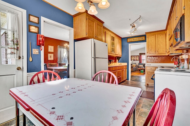 kitchen with track lighting, a notable chandelier, white appliances, backsplash, and sink