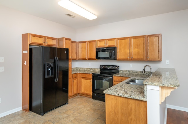 kitchen with light stone countertops, black appliances, sink, a kitchen bar, and kitchen peninsula