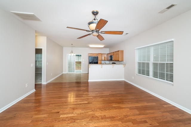 unfurnished living room featuring ceiling fan with notable chandelier and dark wood-type flooring