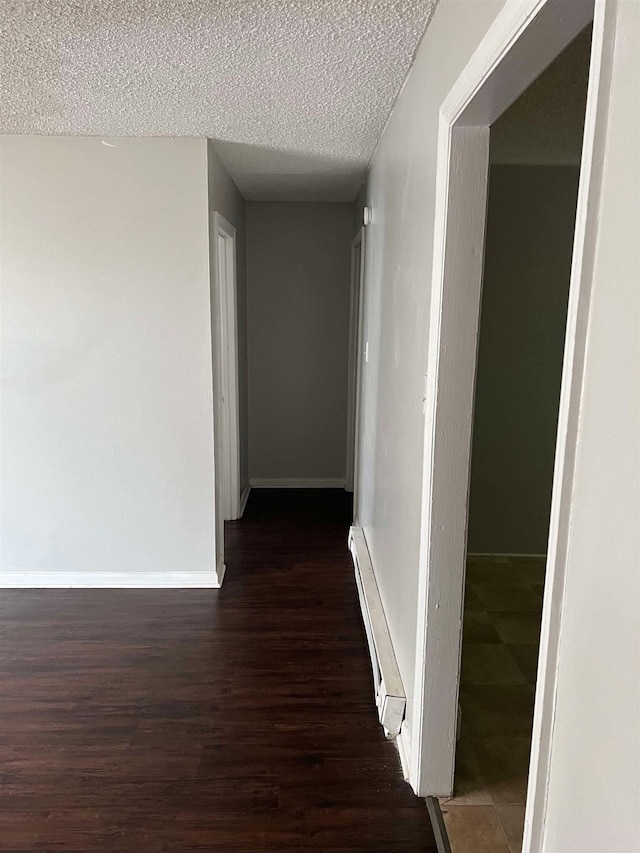 corridor featuring a baseboard heating unit, a textured ceiling, and dark hardwood / wood-style floors