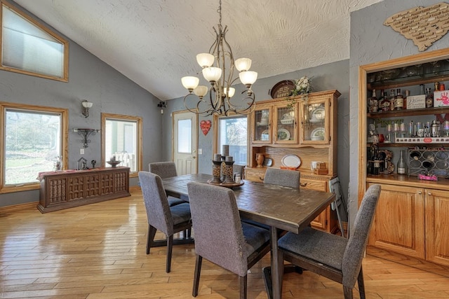 dining area featuring an inviting chandelier, light hardwood / wood-style floors, lofted ceiling, and a textured ceiling