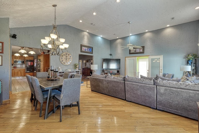 dining area featuring light wood-type flooring, high vaulted ceiling, a textured ceiling, and ceiling fan with notable chandelier