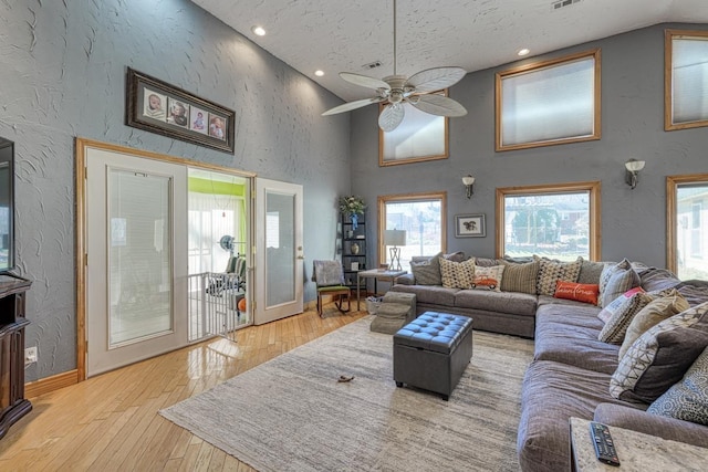 living room with a high ceiling, ceiling fan, and light hardwood / wood-style flooring