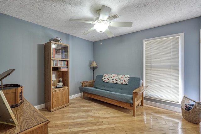 living area with light hardwood / wood-style floors, ceiling fan, and a textured ceiling