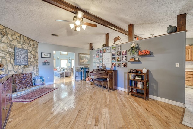 interior space with light wood-type flooring, ceiling fan, lofted ceiling with beams, and a textured ceiling