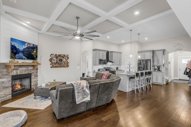 living room with coffered ceiling, dark wood-type flooring, ceiling fan, and a fireplace