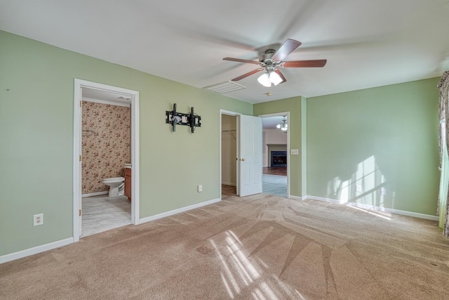 unfurnished bedroom featuring a closet, connected bathroom, ceiling fan, light carpet, and a walk in closet