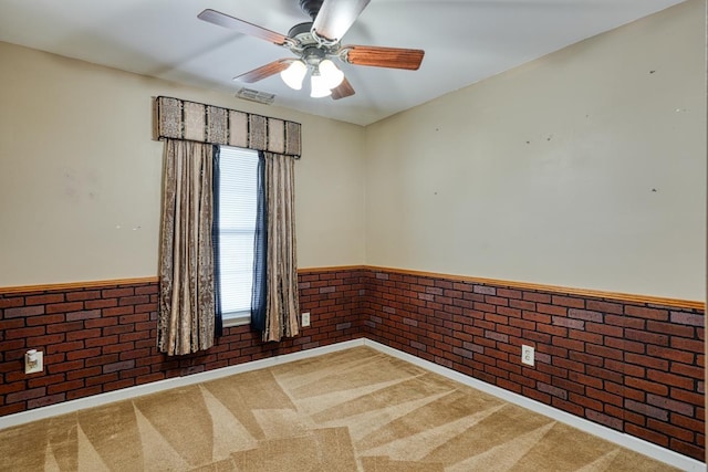 carpeted spare room with ceiling fan and brick wall