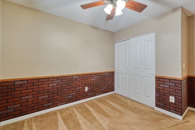 unfurnished bedroom featuring a closet, ceiling fan, brick wall, and light colored carpet