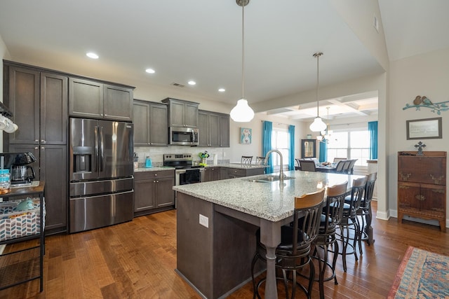 kitchen featuring hanging light fixtures, stainless steel appliances, light stone countertops, sink, and a kitchen breakfast bar