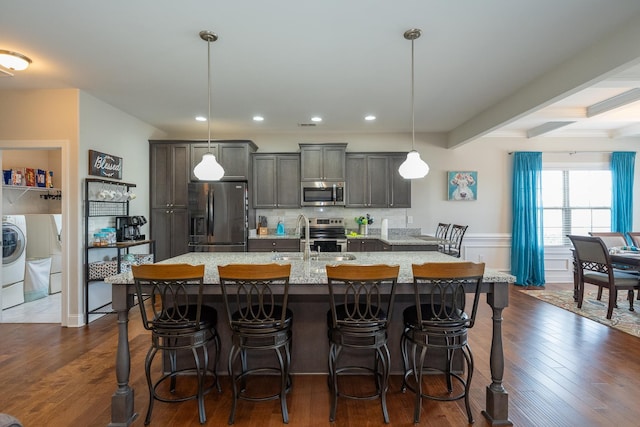 kitchen featuring a kitchen bar, sink, pendant lighting, stainless steel appliances, and an island with sink
