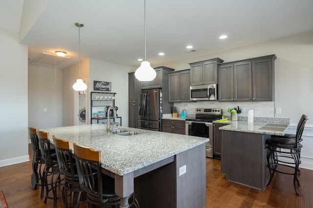 kitchen with a kitchen island with sink, hanging light fixtures, sink, light stone counters, and appliances with stainless steel finishes