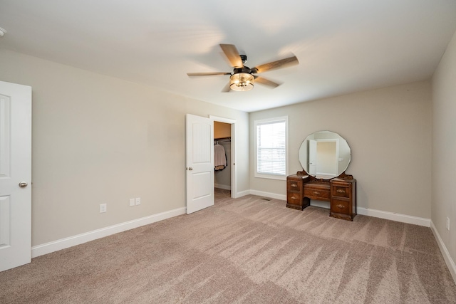 unfurnished bedroom with light carpet, a walk in closet, and ceiling fan