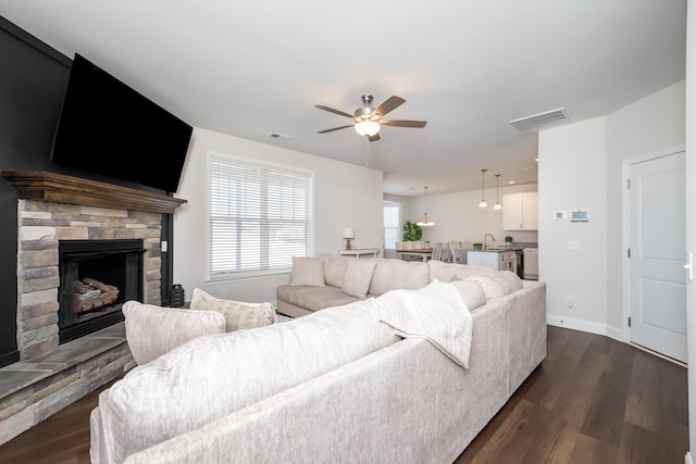 living room featuring sink, a stone fireplace, dark hardwood / wood-style floors, and ceiling fan