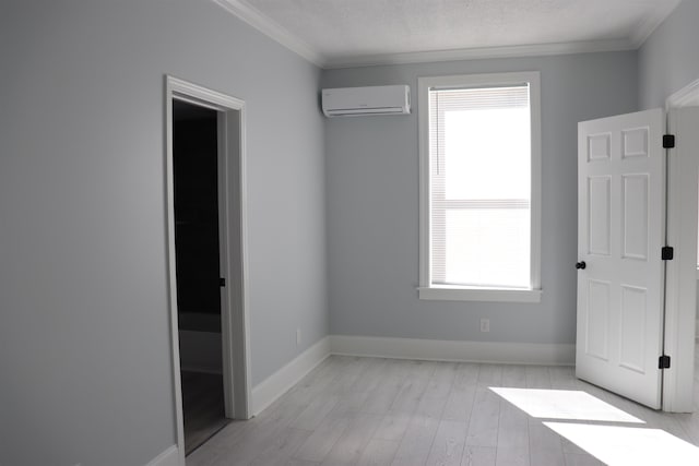 unfurnished bedroom with light wood-type flooring, a wall mounted AC, multiple windows, and a textured ceiling
