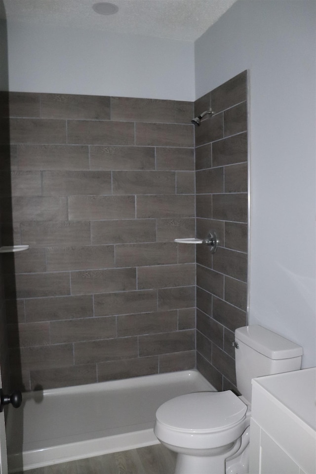 bathroom with wood-type flooring, toilet, a tile shower, a textured ceiling, and vanity