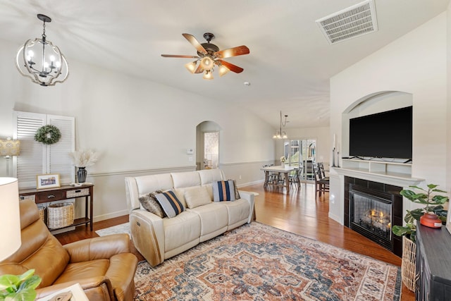 living room featuring ceiling fan with notable chandelier, lofted ceiling, a tile fireplace, and wood-type flooring