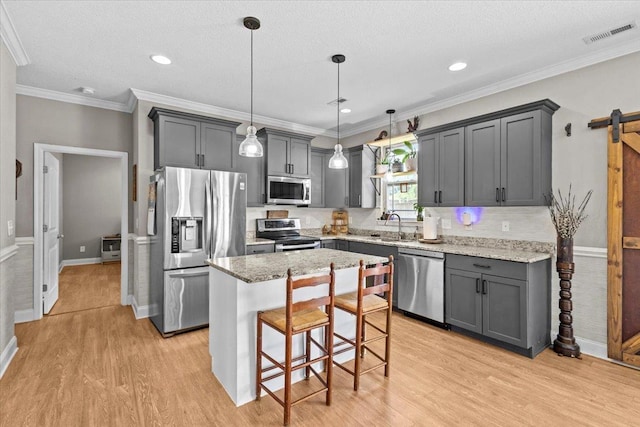 kitchen featuring a kitchen island, gray cabinets, appliances with stainless steel finishes, a kitchen breakfast bar, and pendant lighting