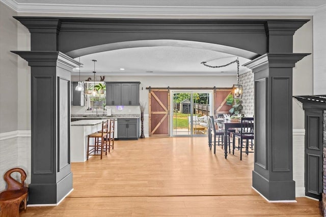 dining room featuring light wood-type flooring, crown molding, decorative columns, and a barn door