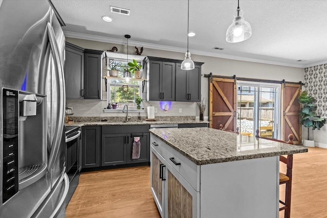 kitchen with a barn door, decorative light fixtures, a kitchen island, light stone counters, and appliances with stainless steel finishes