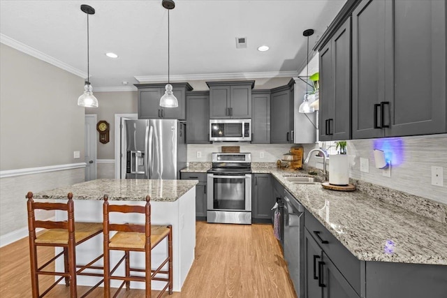 kitchen with appliances with stainless steel finishes, sink, a center island, pendant lighting, and light wood-type flooring