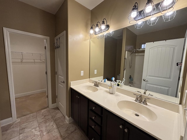 full bath with double vanity, a spacious closet, a sink, and baseboards