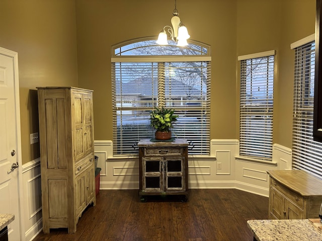 dining room featuring dark wood-type flooring, a chandelier, a healthy amount of sunlight, and wainscoting