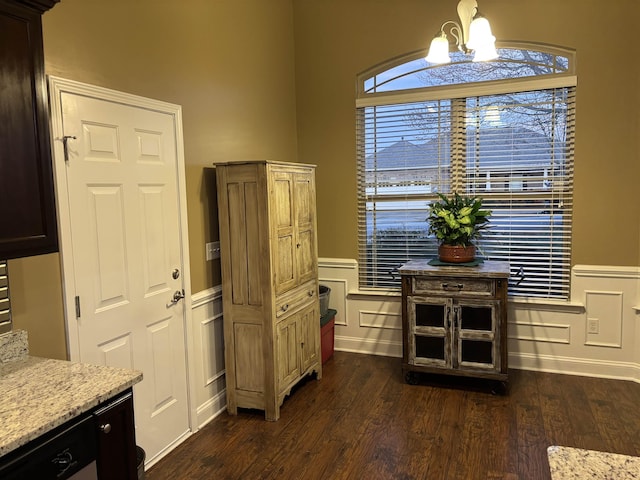 interior space with dark wood-style floors, a wainscoted wall, an inviting chandelier, and light stone countertops