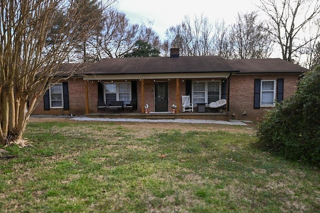 single story home featuring covered porch, brick siding, a chimney, and a front lawn