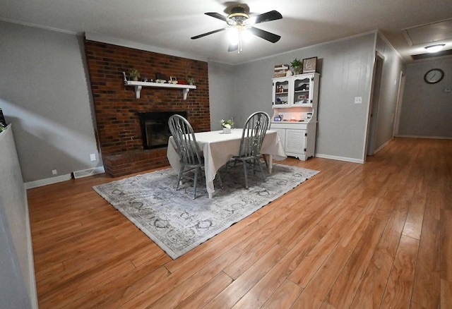 dining room with light wood-type flooring, a fireplace, ornamental molding, and a ceiling fan