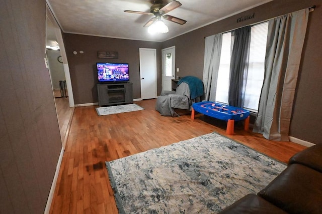 living room with baseboards, crown molding, a ceiling fan, and wood finished floors