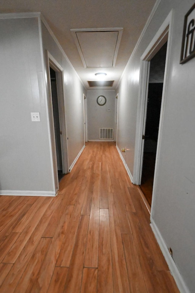 hall with attic access, baseboards, visible vents, light wood-style flooring, and ornamental molding