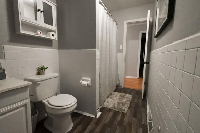 bathroom with wainscoting, toilet, wood finished floors, vanity, and tile walls