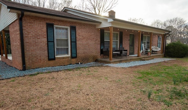 rear view of property featuring brick siding, a yard, and a chimney