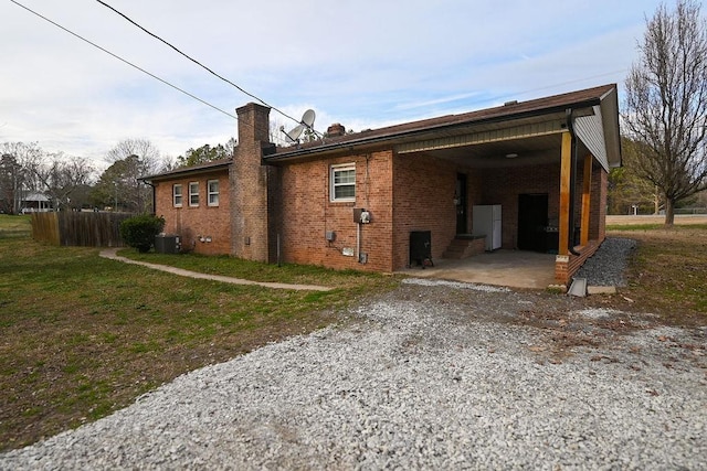 rear view of property featuring driveway, brick siding, a lawn, and cooling unit