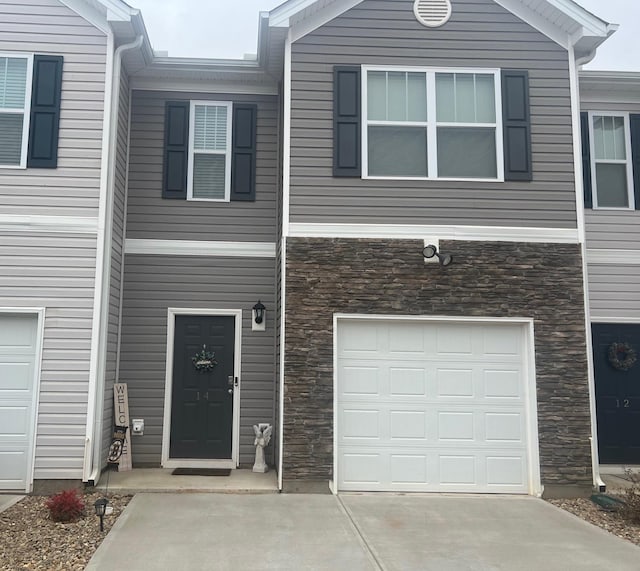 townhome / multi-family property with an attached garage, stone siding, and concrete driveway