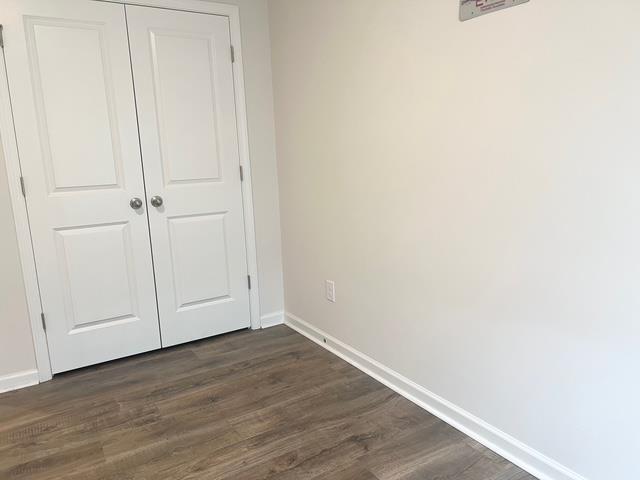 unfurnished bedroom featuring a closet, dark wood finished floors, and baseboards
