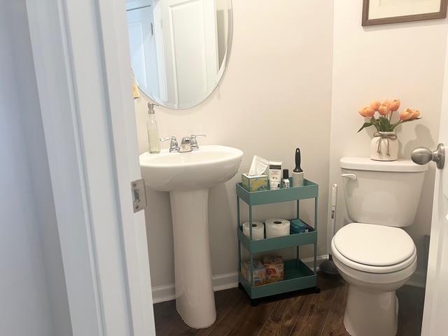 half bathroom featuring baseboards, toilet, and wood finished floors