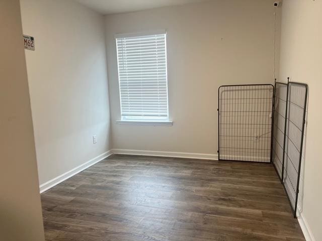 spare room with baseboards and dark wood-type flooring