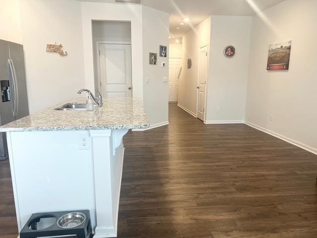 kitchen with stainless steel fridge, dark wood finished floors, a breakfast bar area, light stone counters, and a sink