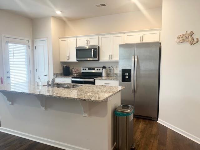 kitchen featuring stainless steel appliances, a breakfast bar, a sink, visible vents, and white cabinetry