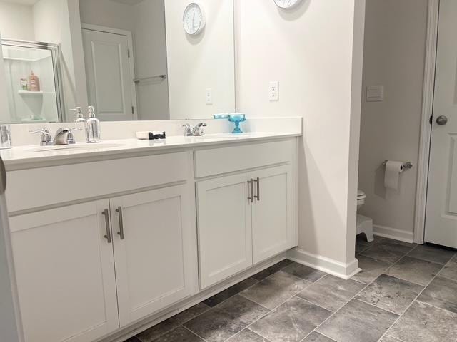 bathroom featuring double vanity, a sink, toilet, and baseboards