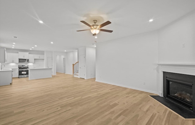 unfurnished living room with light wood finished floors, a fireplace with flush hearth, stairs, and recessed lighting