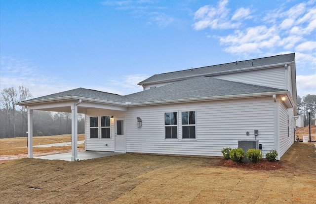 rear view of property with central air condition unit, roof with shingles, a lawn, and a patio